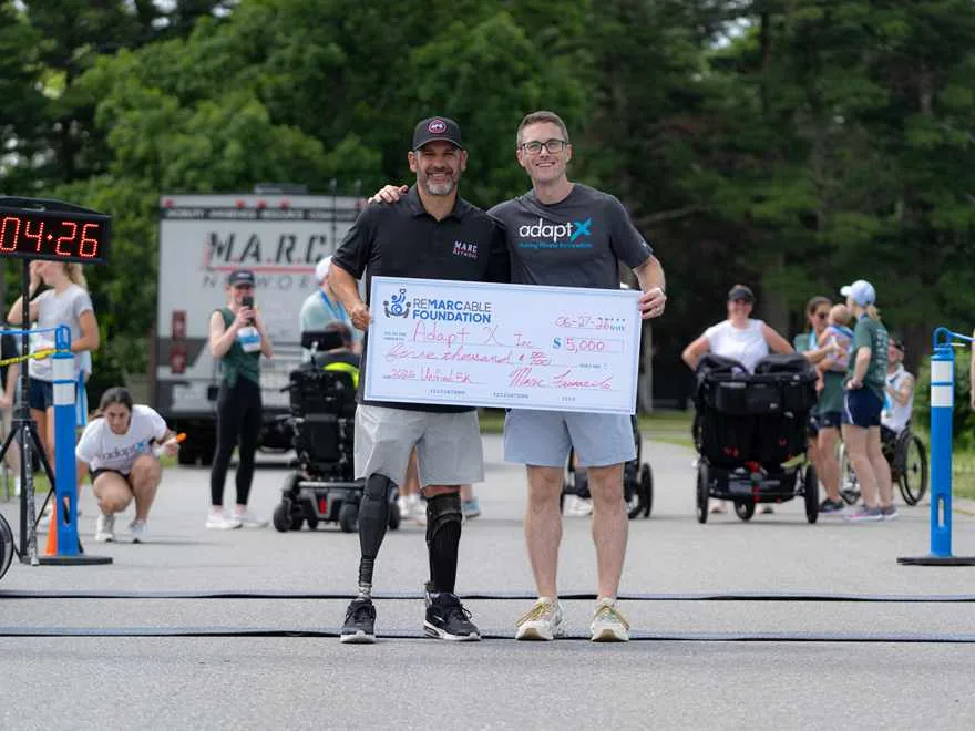 Brendan Aylward and a supporter holding an oversized cheque for five thousand dollars from the ReMARCable Foundation, made out to AdaptX Inc, at the finish of the 2026 Unified 5K