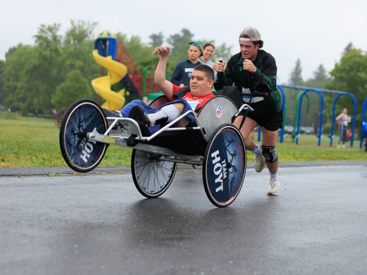Two runners pushing a rider through the rain, the rider punching one fist into the air