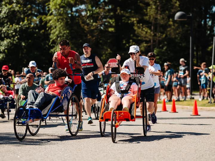Several duo teams racing side by side on a coned road, a field of runners following behind