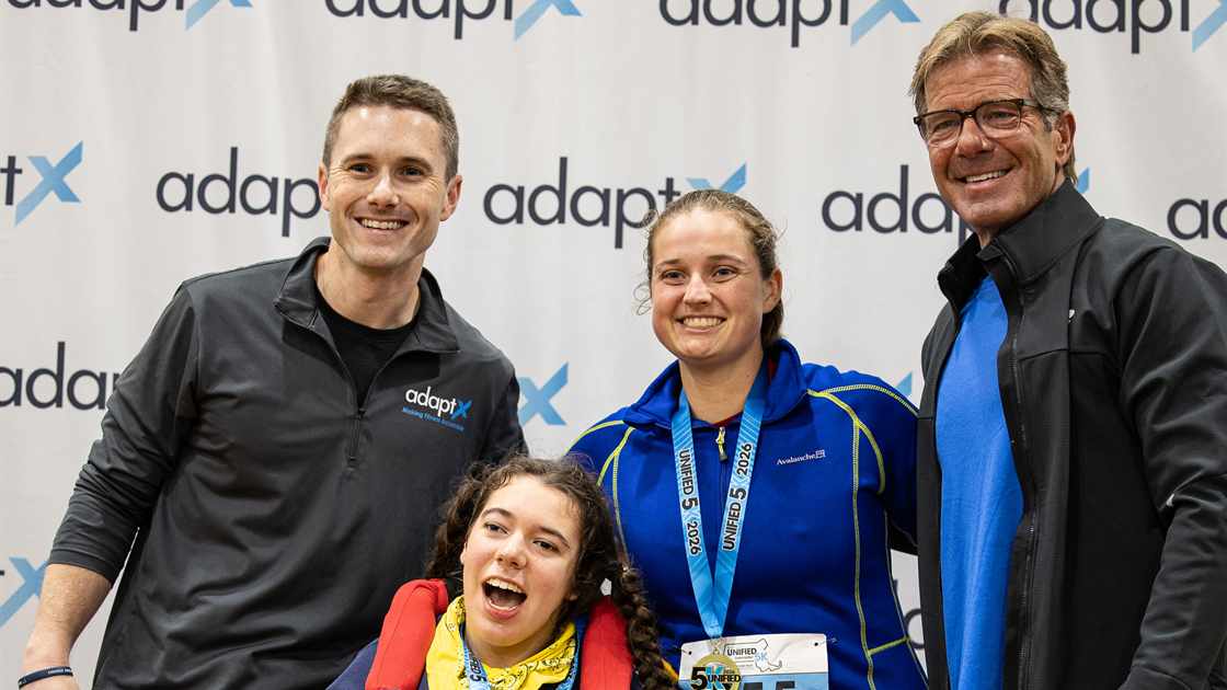 Brendan Aylward, Maeve, Meghan and Mark together in front of an adaptX backdrop, Maeve in her wheelchair and Meghan wearing a Unified 5K 2026 medal