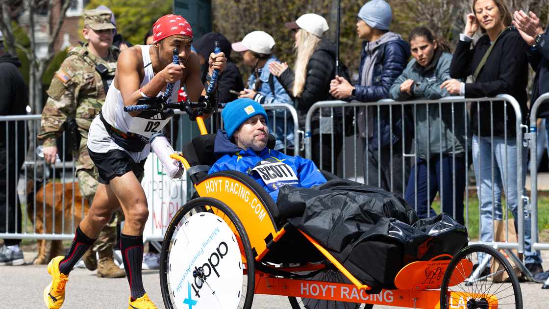 Tatsuya pushing Scott in an orange Hoyt racing chair at the Boston Marathon