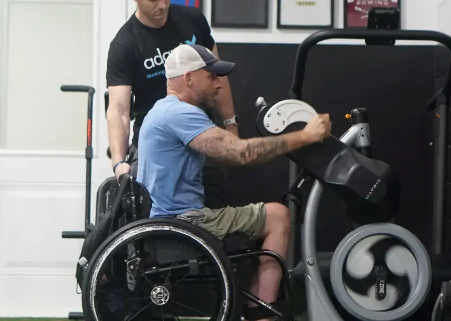 A wheelchair user training on gym equipment with a coach