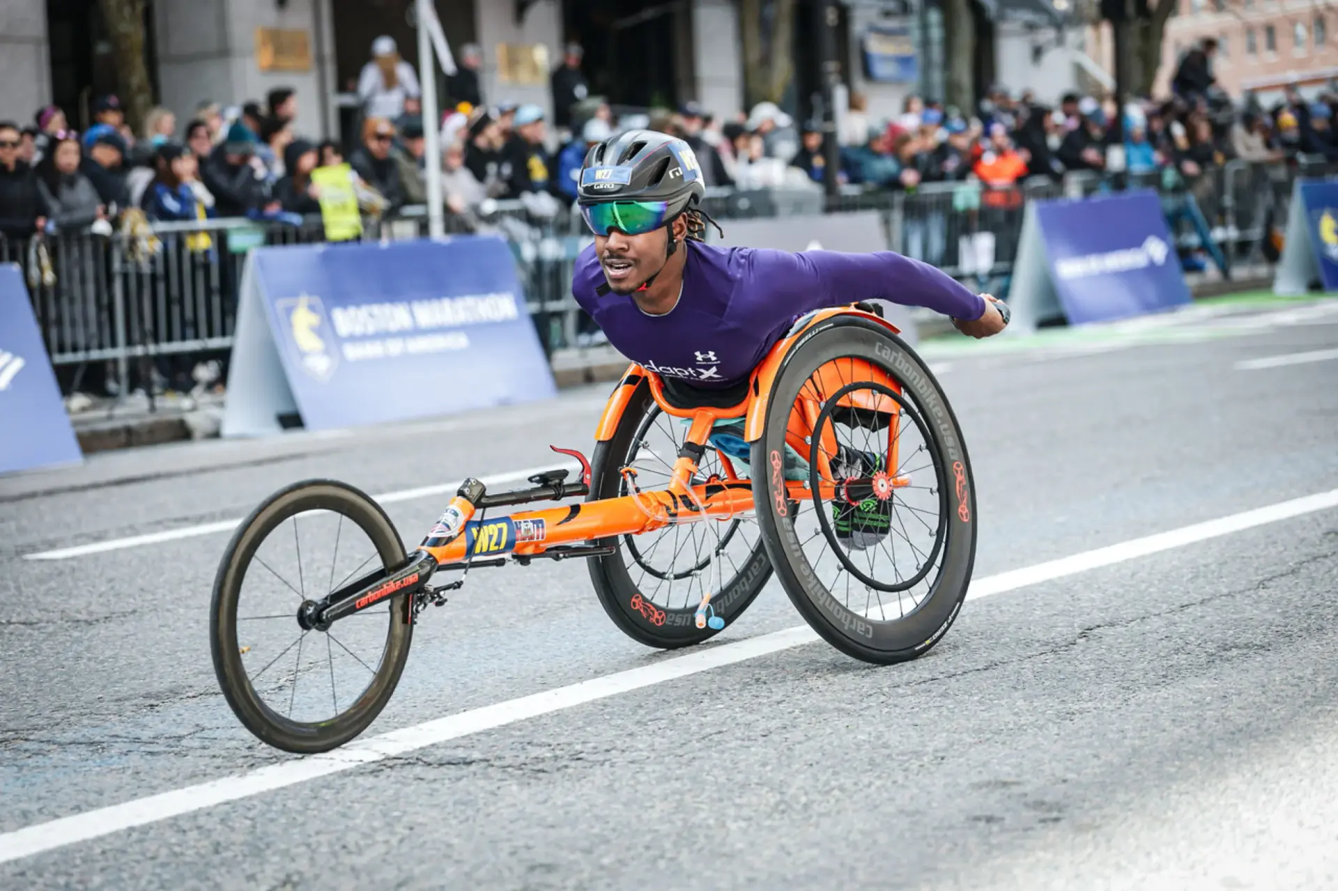 A wheelchair racer in an orange racing chair on the Boston Marathon course