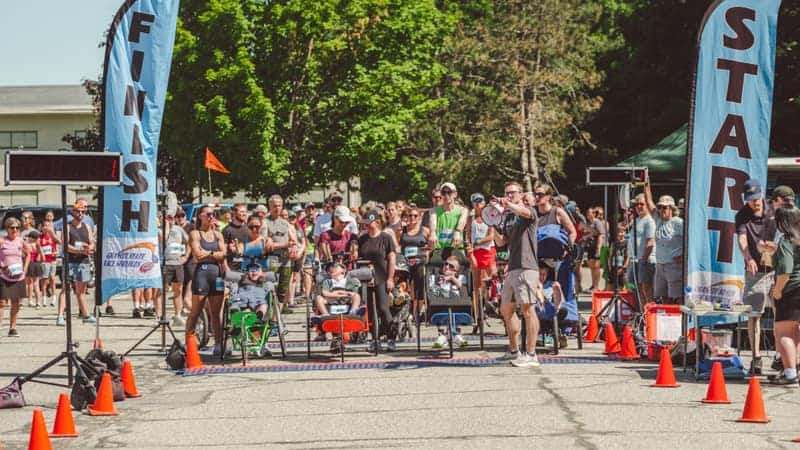A crowd of runners, handcyclists and racing chairs packed between START and FINISH flags at the start of a race on a coned road.