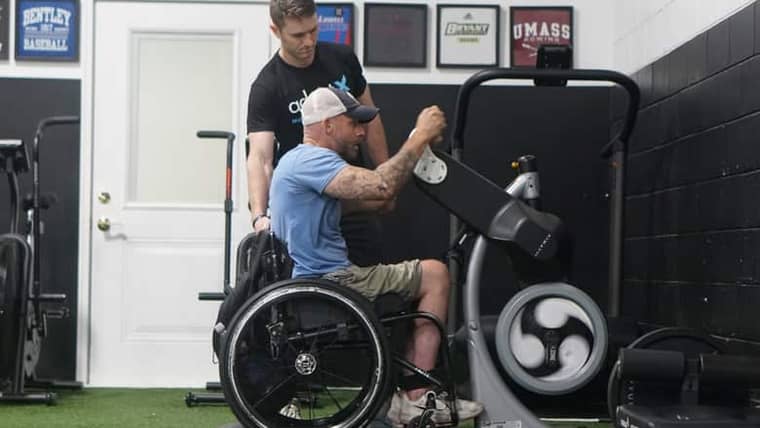 A coach working with a wheelchair user at an arm cycle in the gym.