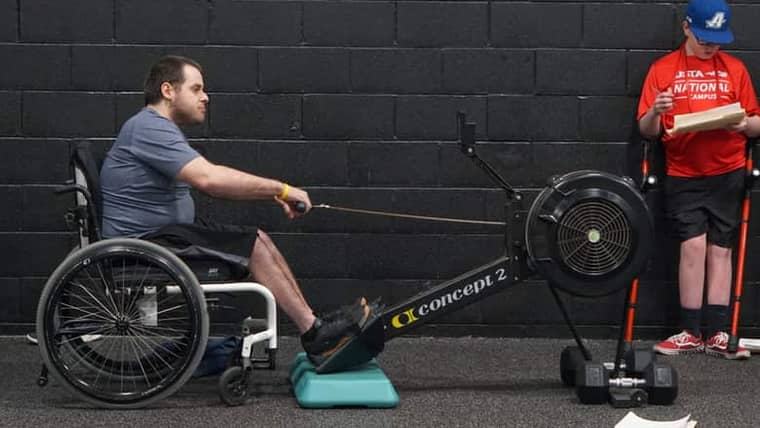 A wheelchair user rowing on an adapted erg in the gym.