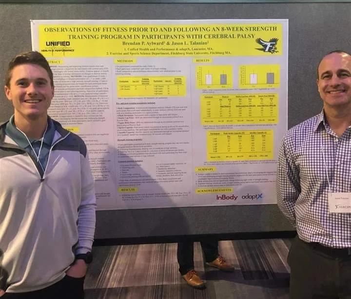 Two authors standing in front of their research poster on the effects of strength and conditioning for people with cerebral palsy