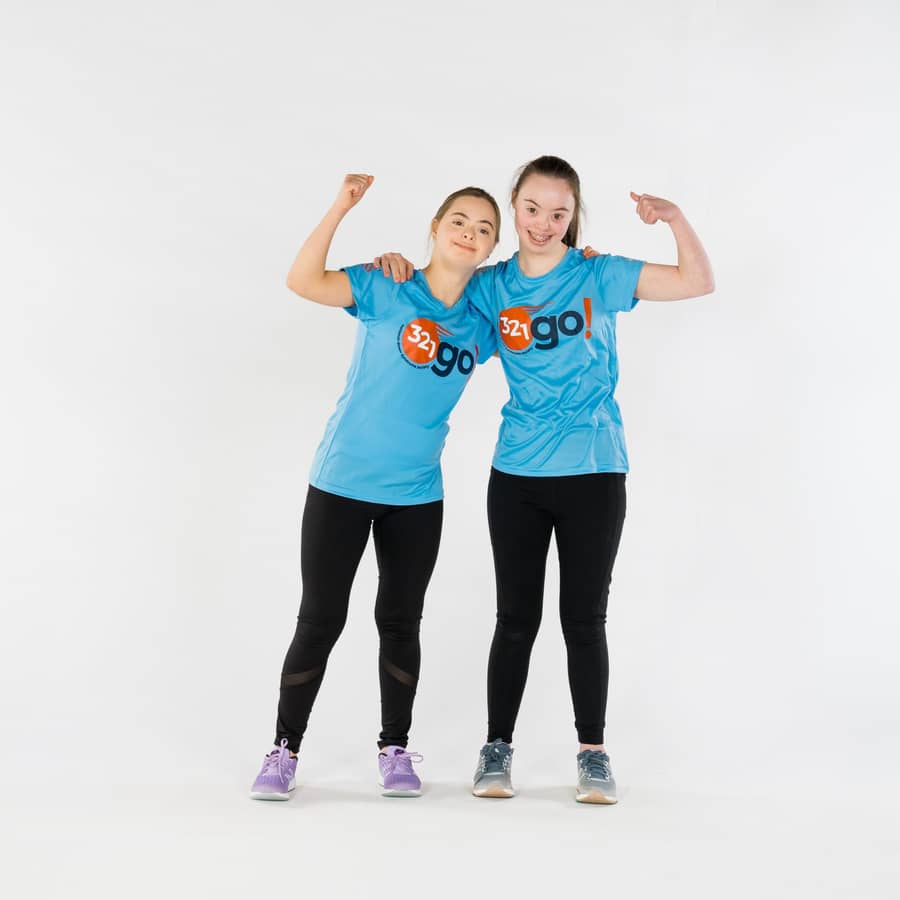Two young women in blue 321go! t-shirts standing arm in arm and flexing their biceps.