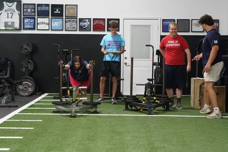 The gym floor during a session, with athletes and coaches spread across the turf and the racks.