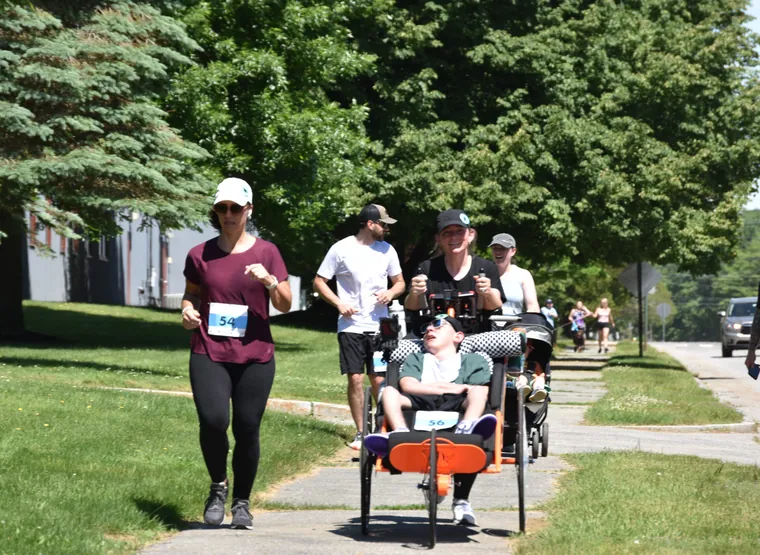A runner pushing a duo chair along the shaded course