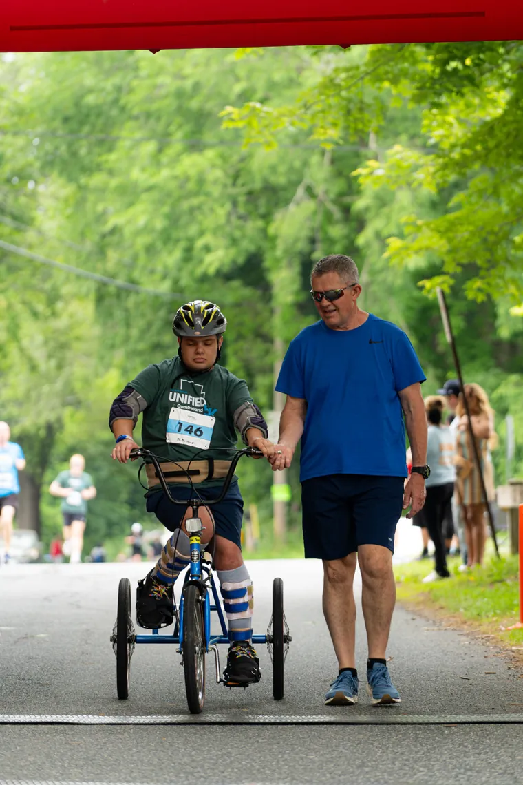 A child on an adaptive trike running the course alongside an adult