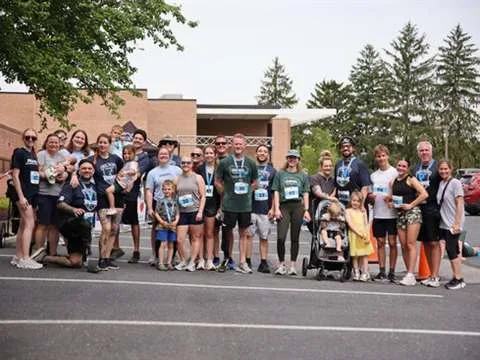A large group of participants in race shirts posed together outside a brick building