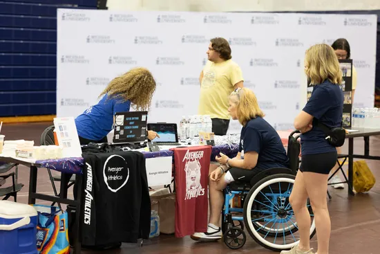 A visitor in a wheelchair talking with exhibitors at a stand