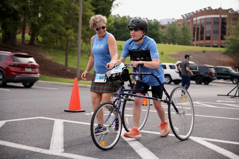 A cyclist walking a bike beside a runner in the car park before the start