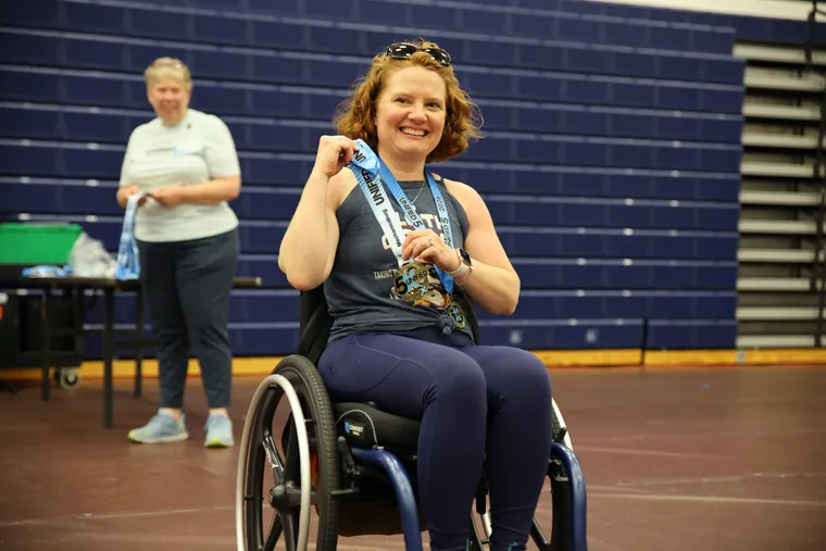 A wheelchair racer holding up her finisher medal in the gym