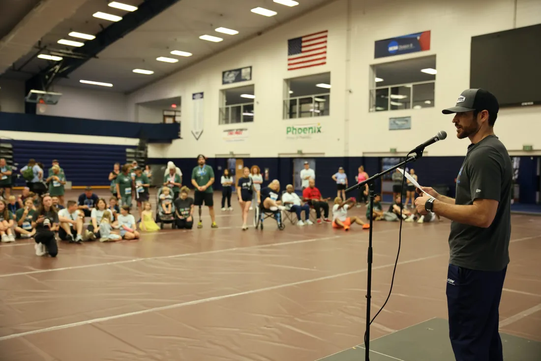A race director addressing participants with a microphone in the Messiah University gym