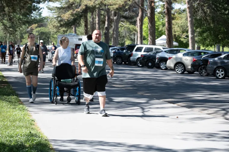 An athlete on a running blade walking the course beside a pushchair