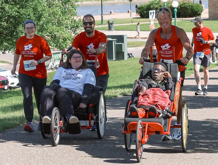 Two duo teams pushing racing chairs along the riverside path