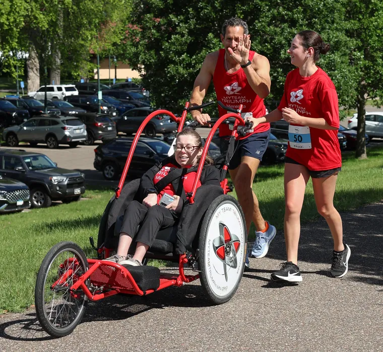 A duo team pushing a red racing chair, the rider smiling