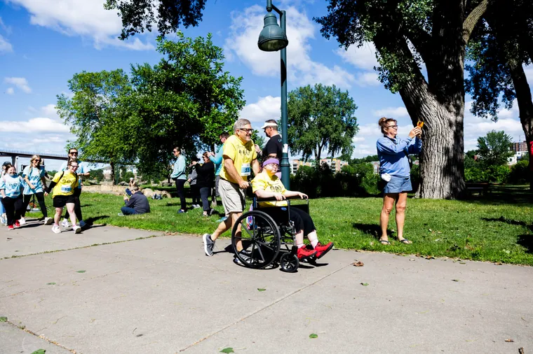 A volunteer pushing a participant in a wheelchair past the crowd