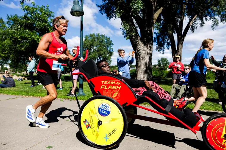 Runners pushing a yellow-wheeled racing chair on the course