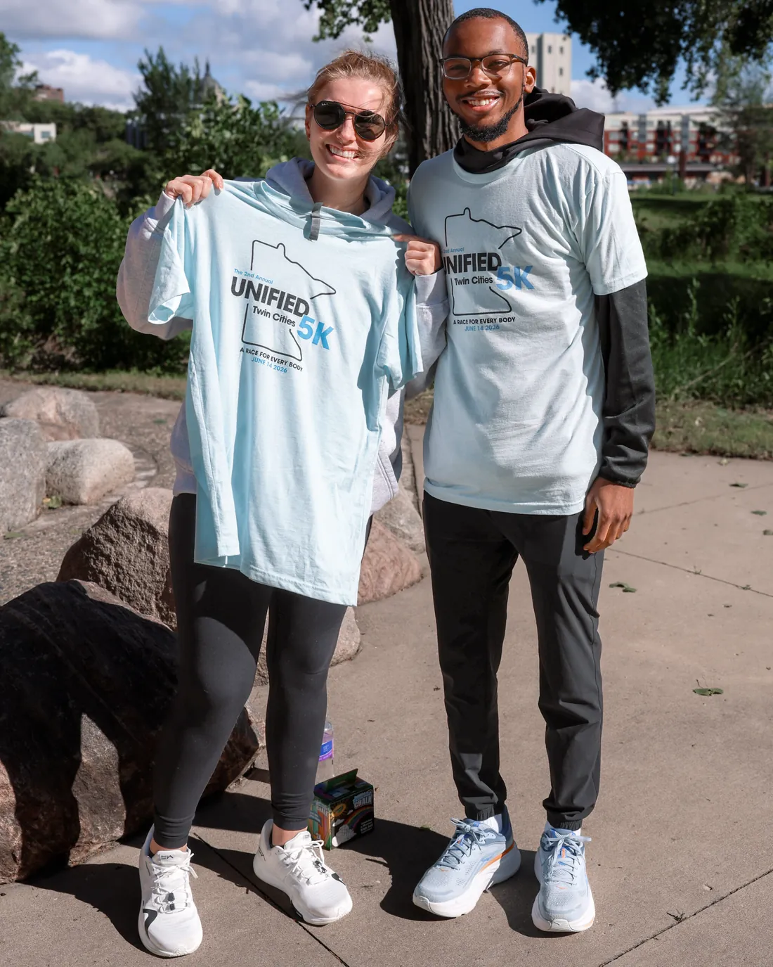 Two volunteers holding up a Unified 5K shirt beside the river