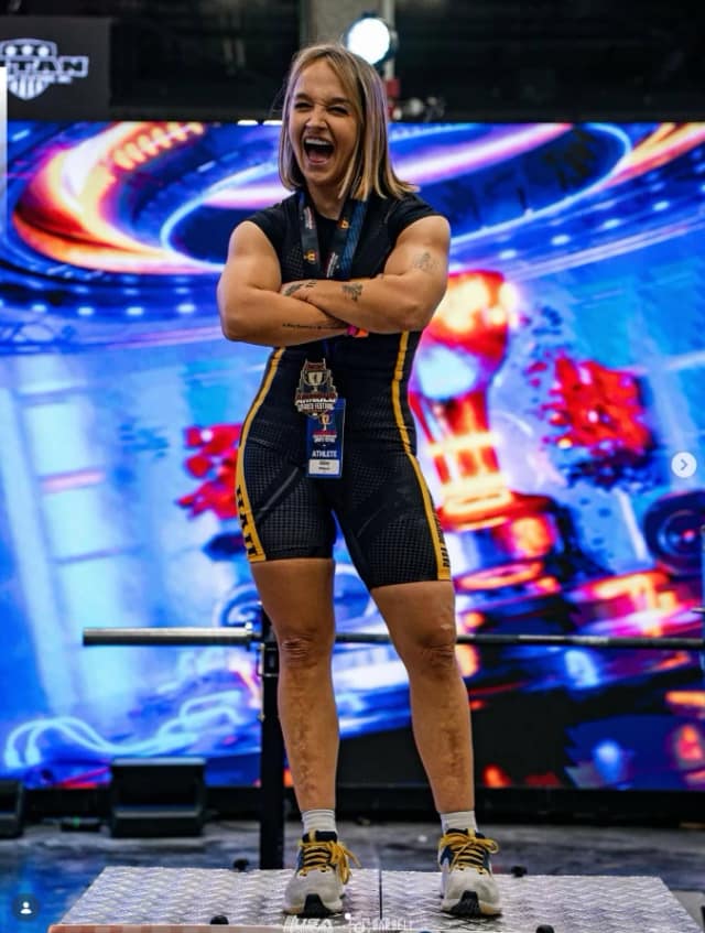 Abbey Phillipson on a powerlifting platform, arms folded and laughing